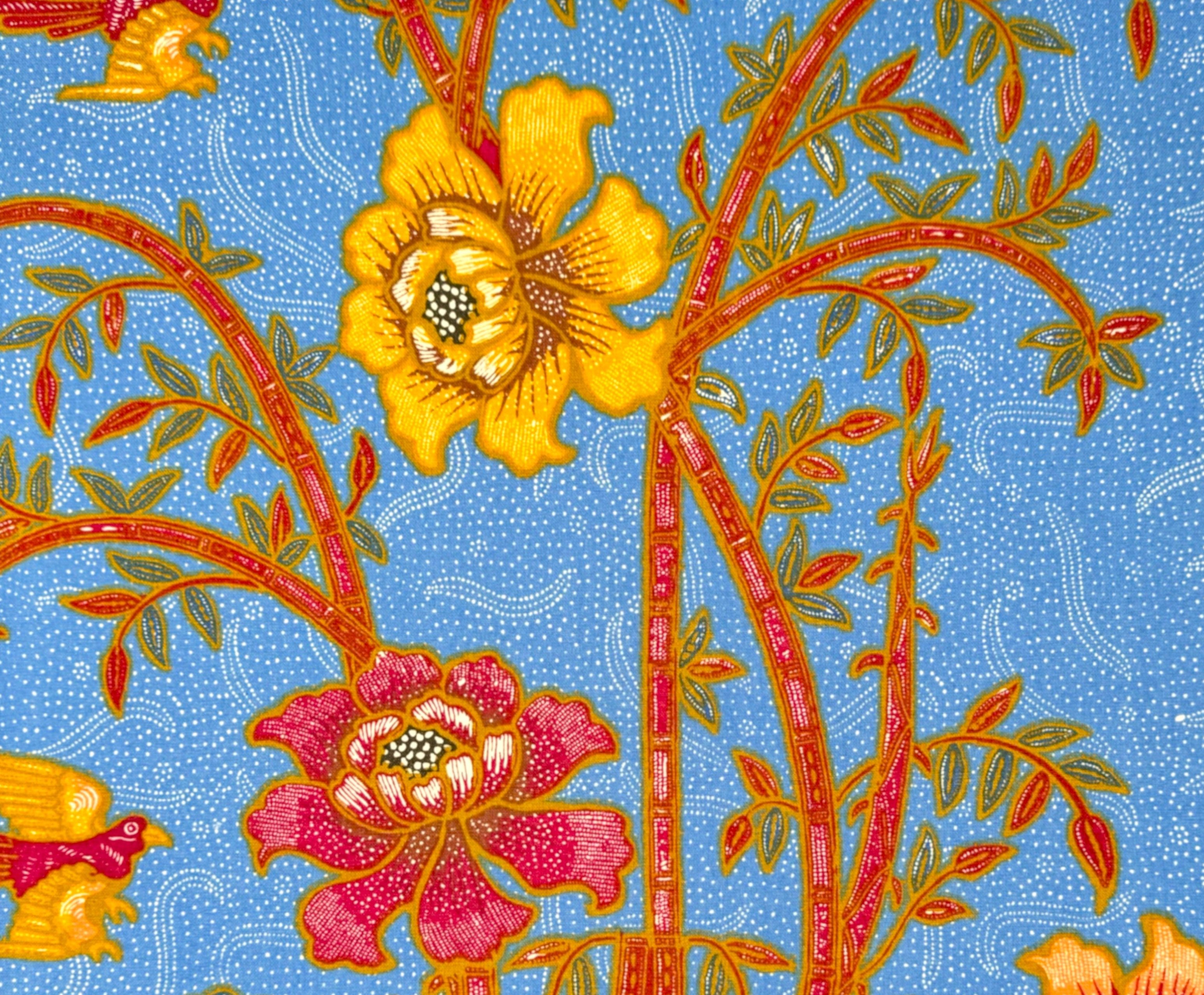 A close-up of a patterned textile or wallpaper featuring stylized flowers and birds on a light blue dotted background. The design includes yellow, orange, pink, and blue floral motifs with red-orange stems and green leaves.